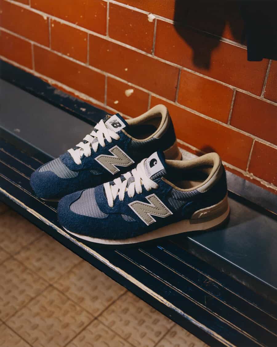 New Balance x Carhartt WIP 990v1 sneaker in navy on a locker room bench