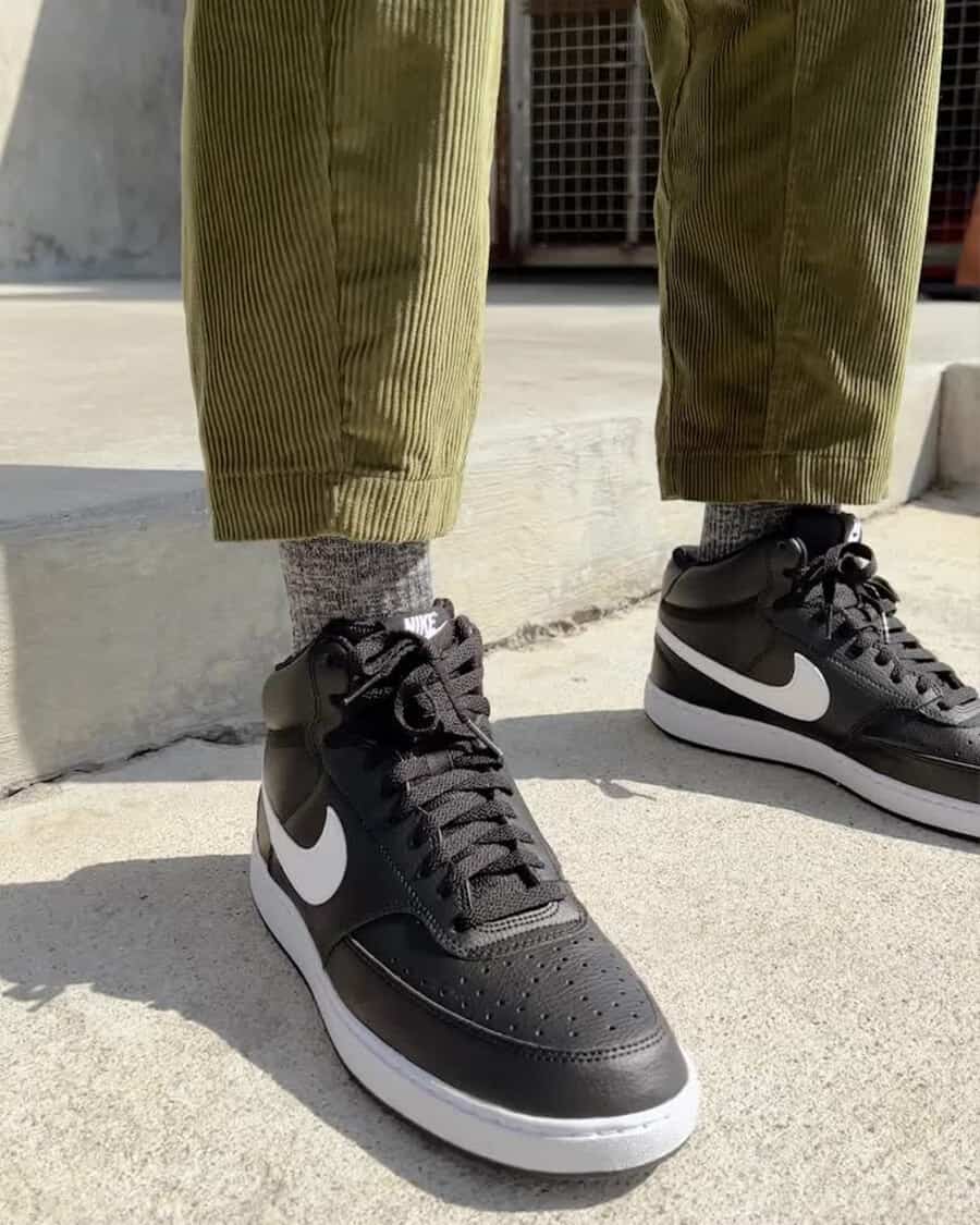 Men's affordable Nike Court Vision Mid sneakers in black worn on feet with grey socks and green corduroy pants