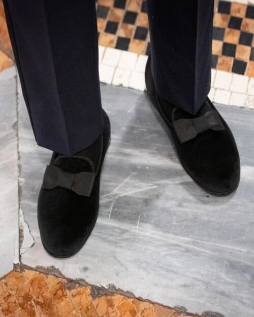 A pair of men's black velvet formal opera pump slippers worn with midnight blue tuxedo trousers