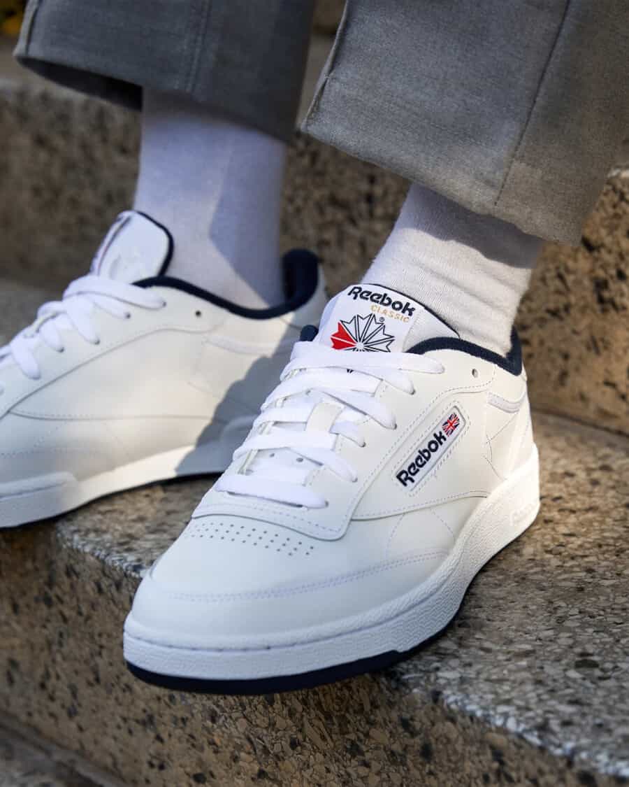 Men's affordable Reebok Club C white sneakers on feet worn with white socks and grey trousers