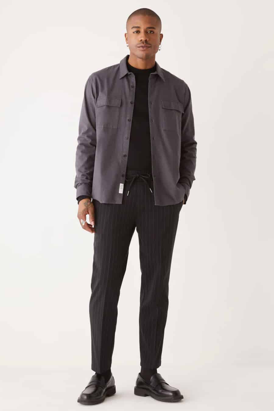 Men's black pinstripe drawstring trousers, black tucked in T-shirt, grey overshirt and black leather penny loafers outfit