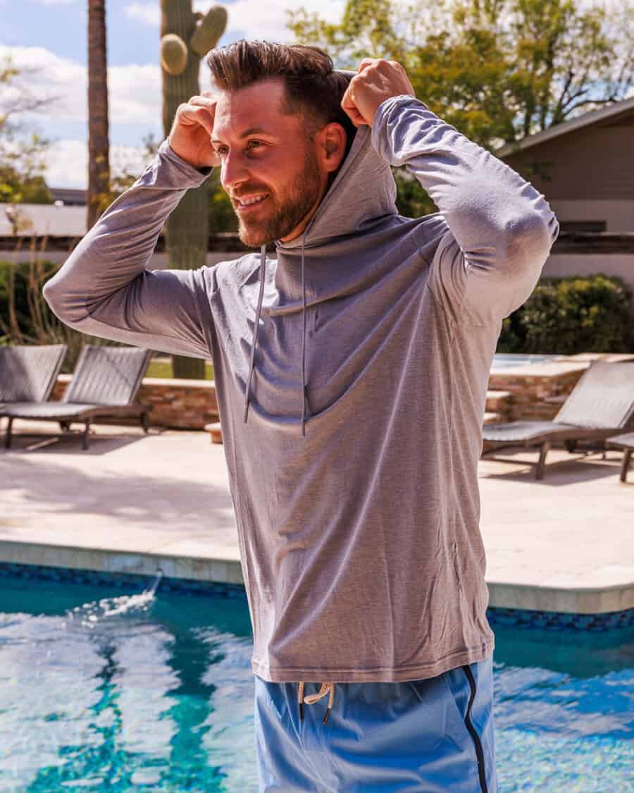 Man wearing a lightweight grey hoodie and bright blue swim shorts next to the pool