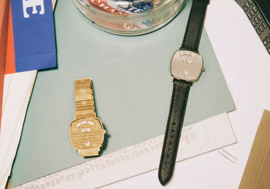 Two Gucci Grip square watches in gold and black leather on a table