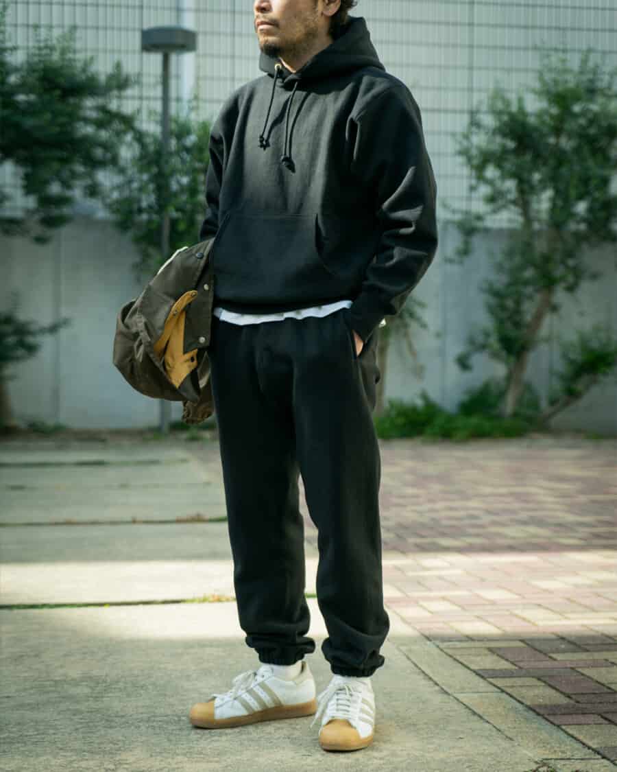 Man wearing The REal McCoy's matching black heavyweight hoodie and sweatpants with white Adidas sneakers