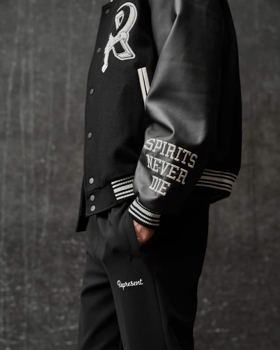 Man wearing black heravyweight Represent sweatpants and a branded black varsity jacket