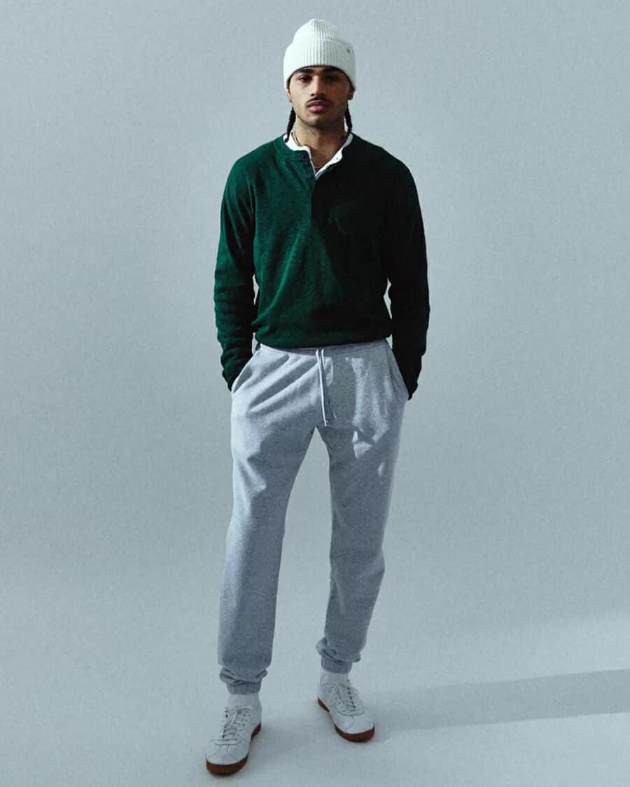 Man wearing tapered heavyweight fleece grey sweatpants by Reigning Champ with a green Henley shirt, white beanie and white sneakers outfit
