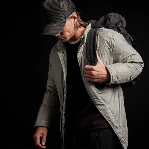 Men's wearing a James Perse long down filled trench coat in light grey over a black sweatshirt with a black baseball cap and backpack