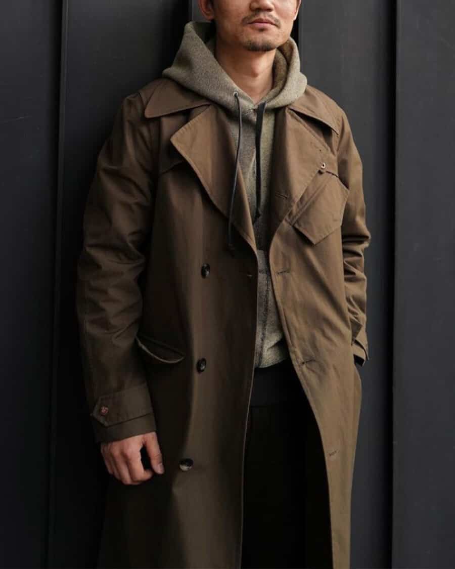 Men's brown trench coat layered over a khaki hoodie