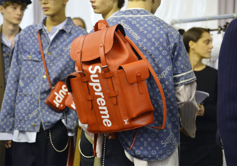 A man wearing a red Supreme backpack worn with a Supreme x Louis Vuitton shirt