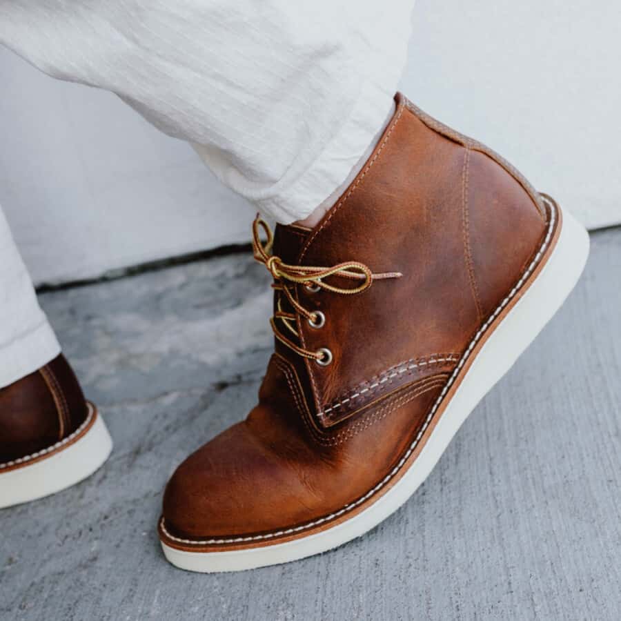 Pair of brown leather Red Wing work boots on feet with white trousers