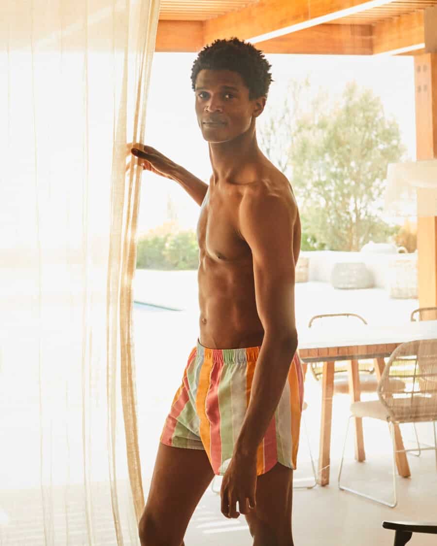 Black man wearing luxury colourful striped boxer shorts by Derek Rose on vacation
