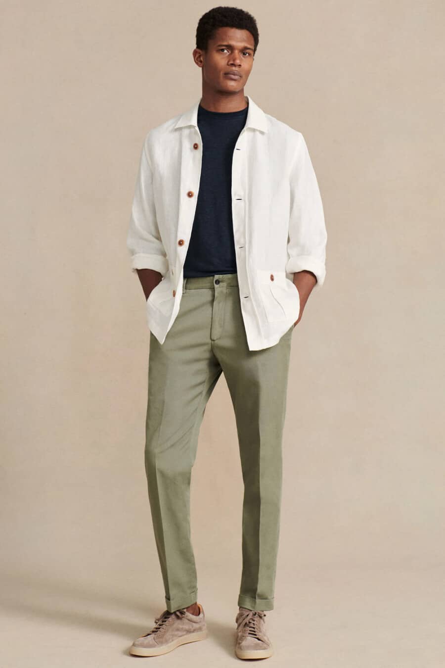 Men's light green tailored pants, tucked in navy T-shirt, open white overshirt and brown suede sneakers outfit