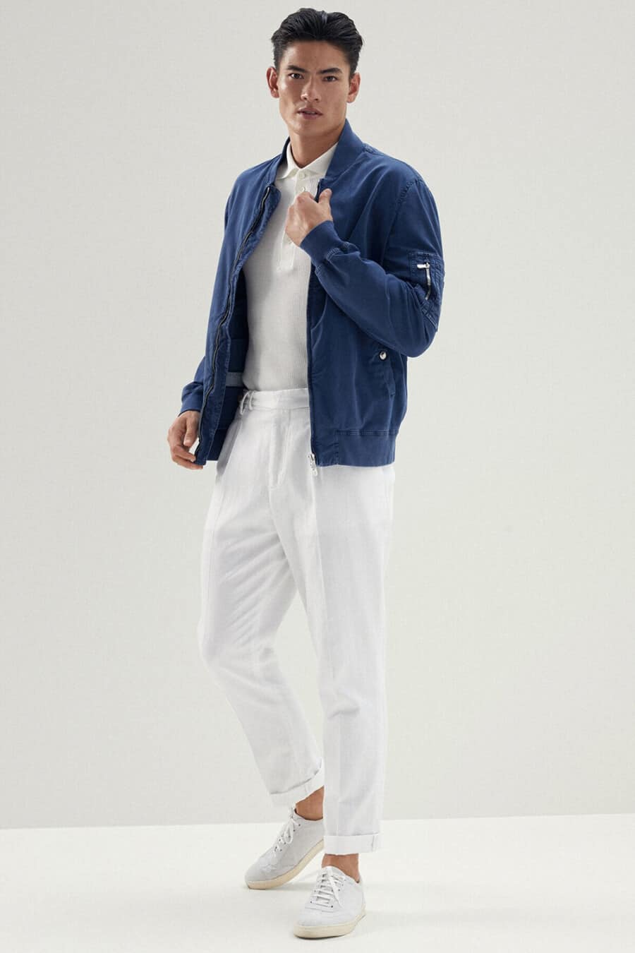 Men's white pants, off-white polo shirt, blue MA-1 bomber jacket and white sneakers outfit