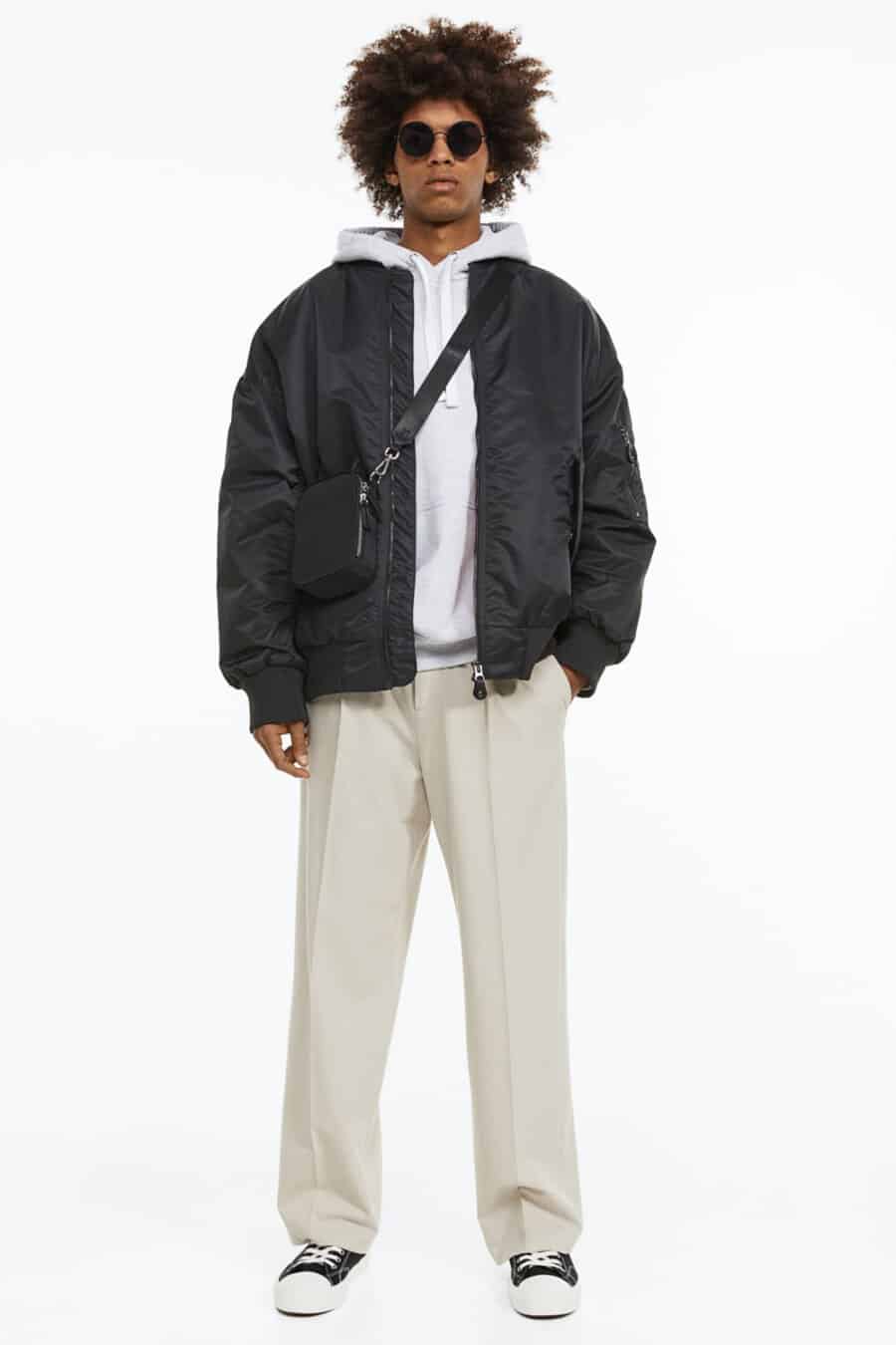 Men's loose off-white pants, grey hoodie, black drop shoulder bomber jacket, black crossbody bag and black canvas sneakers outfit