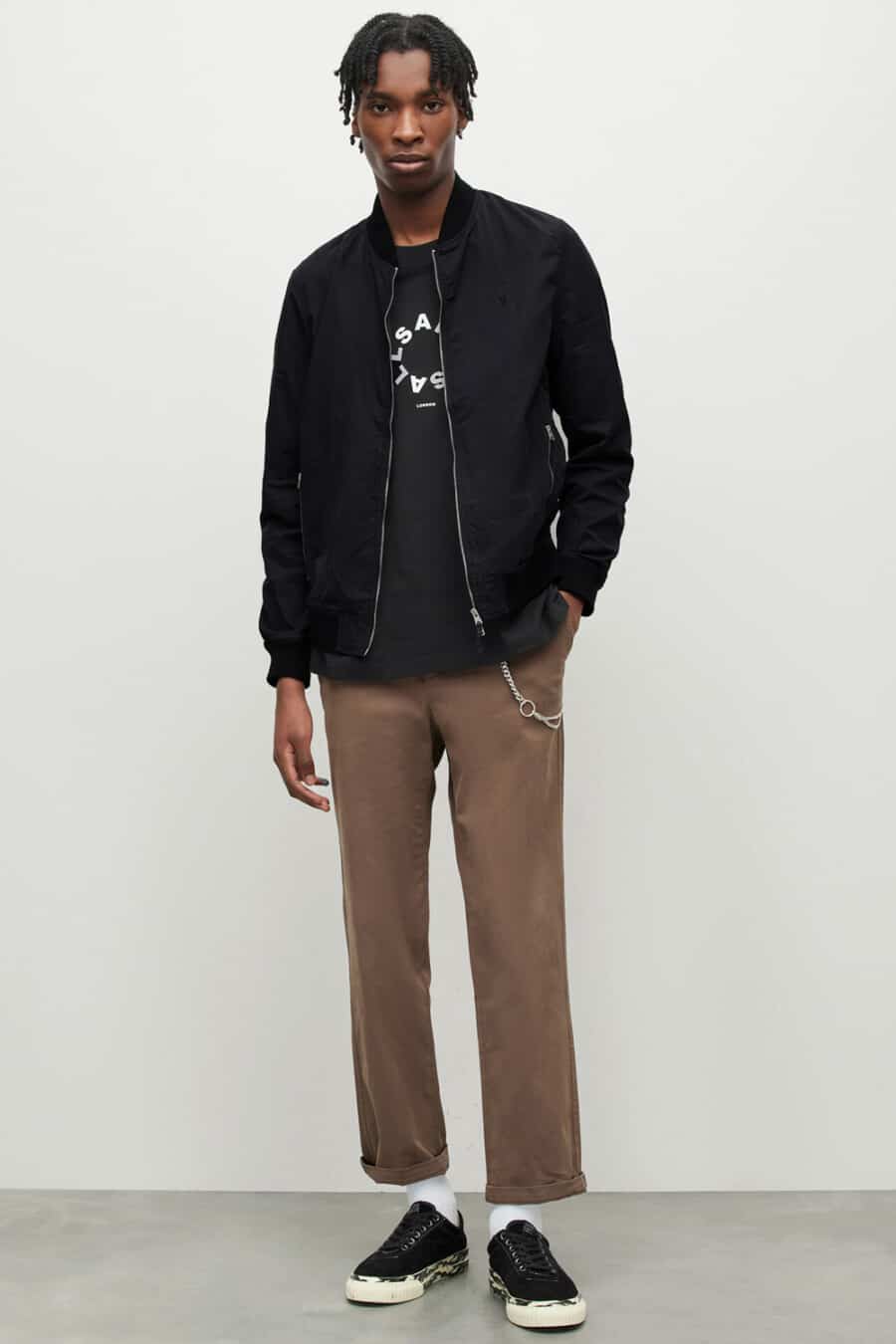 Men's brown pants, black print T-shirt, black bomber jacket, silver wallet chain and black canvas sneakers outfit