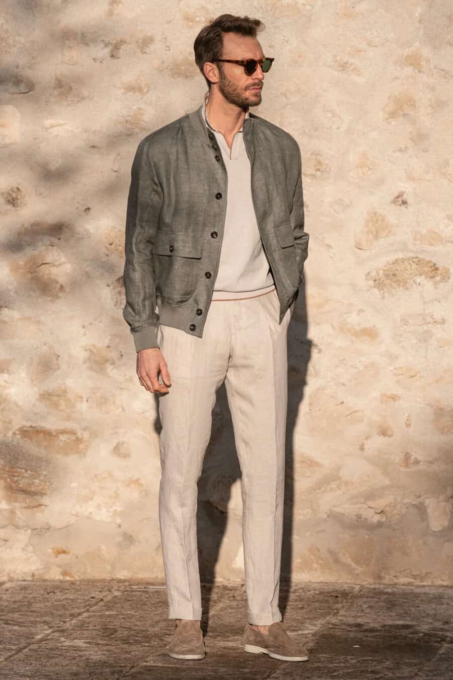 Men's stone linen pants, knitted light grey polo shirt, mid grey linen bomber jacket, tortoiseshell sunglasses and taupe suede loafers outfit