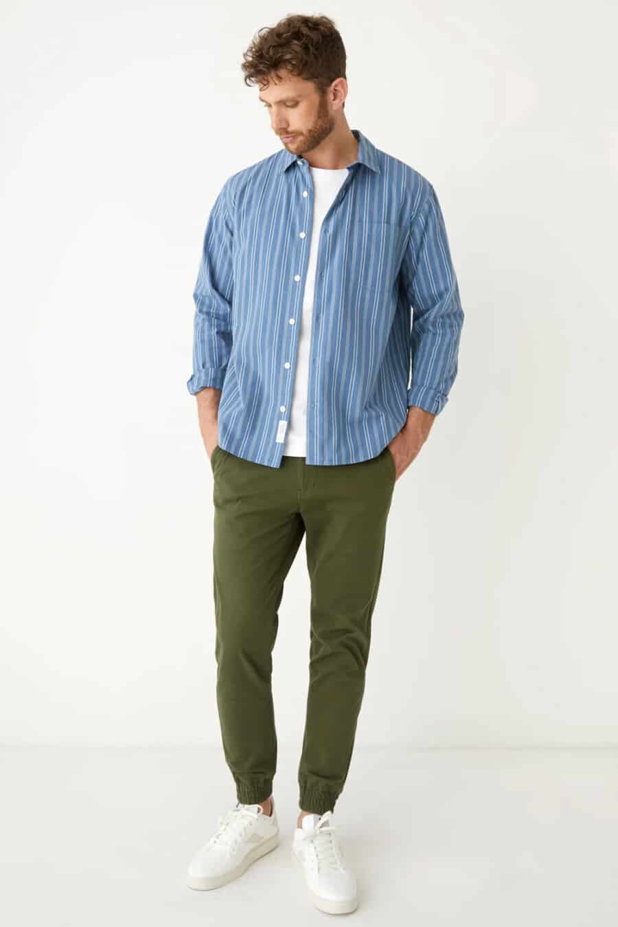 Men's green cuffed pants, white T-shirt, open mid blue striped shirt and white leather sneakers outfit