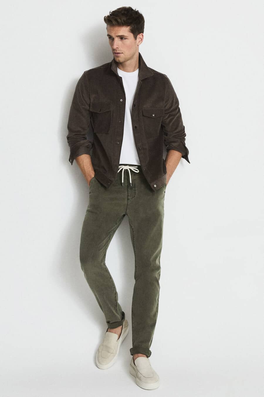 Men's dark green drawstring pants, white T-shirt, brown overshirt and stone suede loafers outfit