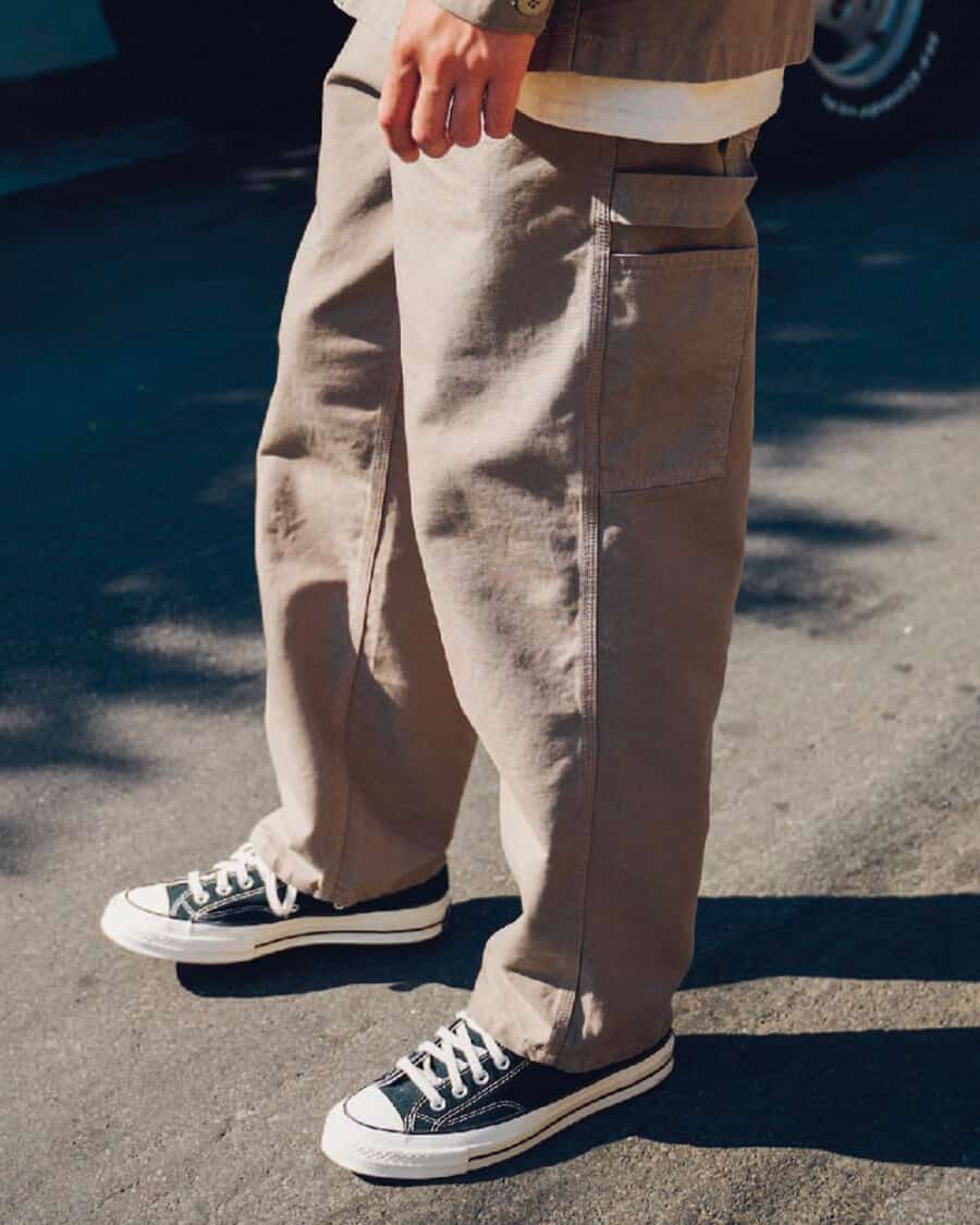Man wearing losse khaki carpenter pants with a white T-shirt and black canvas low top Converse sneakers