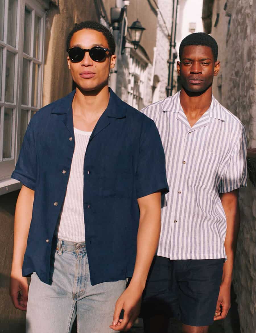 Two black men wearing Cuban collar shirts with shorts and jeans