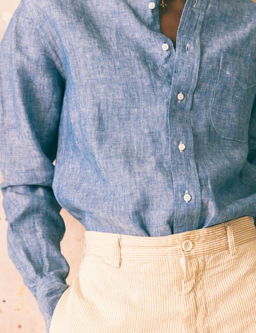 Close up of a man wearing a blue chambray shirt tucked into cream corduroy trousers