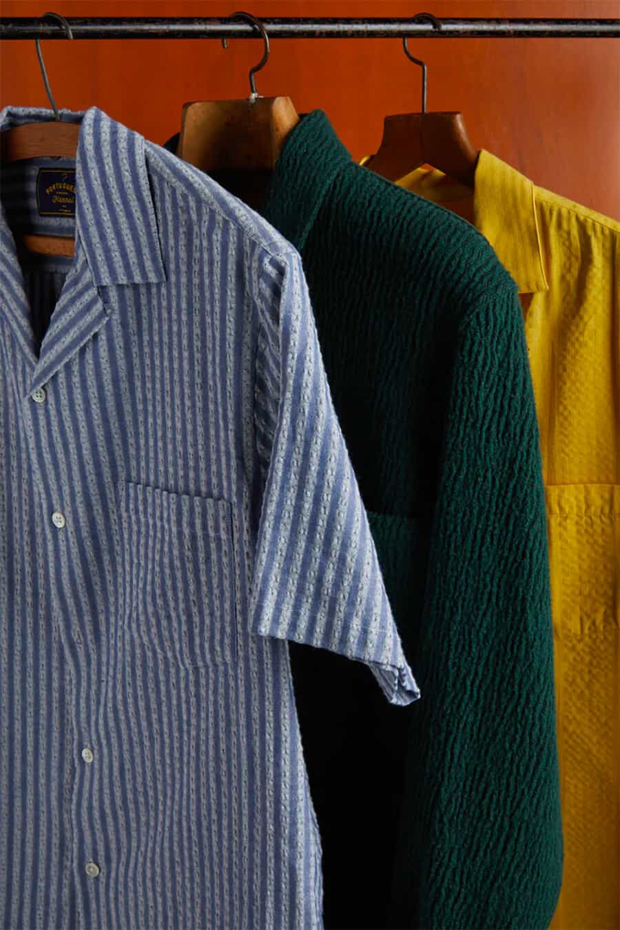 Three seersucker men's summer shirts in yellow, green and blue/white stripe hanging on a clothes rail