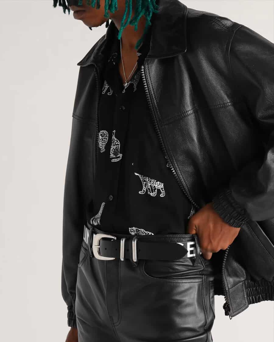 Man wearing black leather pants, black printed shirt, black leather jacket and a luxury black leather logo belt