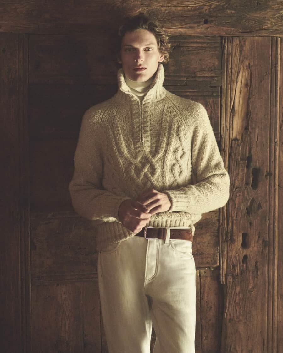 Man wearing luxury Loro Piana white jeans, white roll neck, white zip neck sweater and brown belt