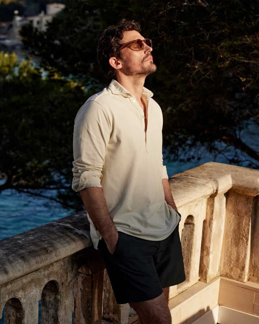 Man wearing a luxury popover white shirt, navy shorts and sunglasses on vacation