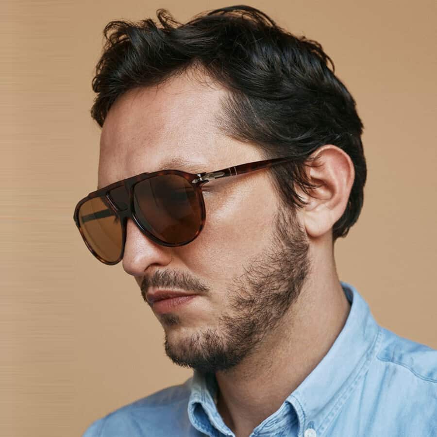 Man wearing oversized, acetate aviator sunglasses on face with sky blue shirt