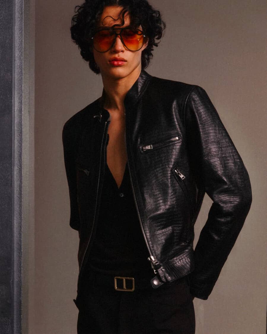 Man wearing Tom Ford black pants, open black shirt, black leather jacket, coloured lens sunglasses and luxury black leather belt