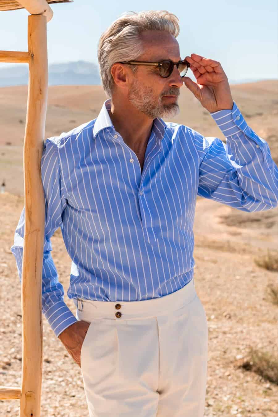 Man wearing off-white tailored pants with a blue/white striped shirt and sunglasses