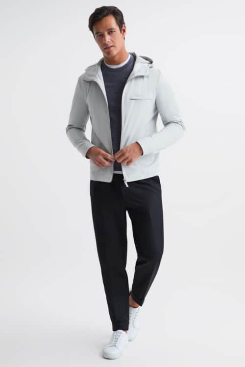 Men's navy pants, white T-shirt, charcoal sweatshirt, light blue technical jacket and white sneakers outfit