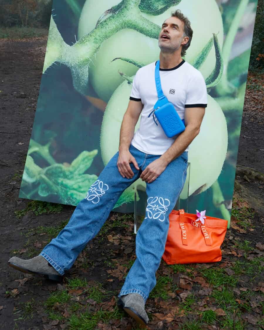 Murray Bartlett wearing a bright blue luxury Loewe crossbody sling bag, embroidered jeans, grey suede shoes and a white T-shirt