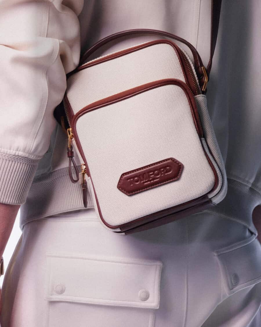 Close up of a man wearing a luxury Tom Ford white crossbody bag with brown leather trim and branding