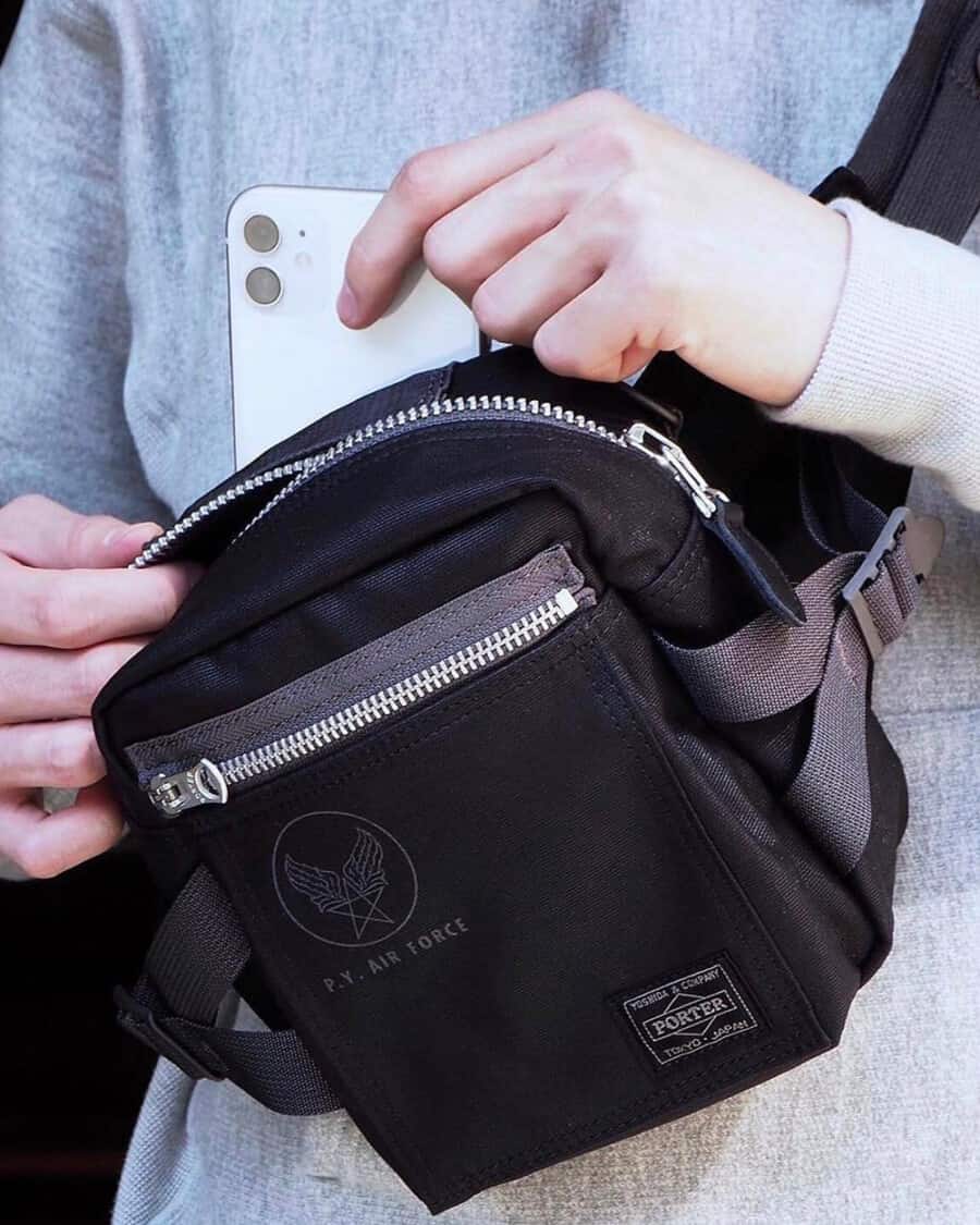 Man putting iPhone in designer Porter Yoshida black crossbody bag