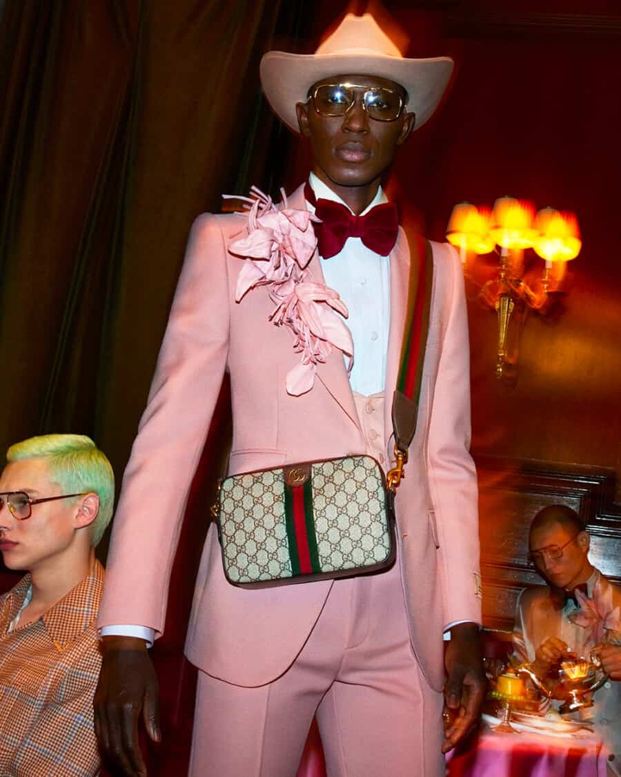 Black model wearing a pink suit and a monogrammed Gucci belt bag