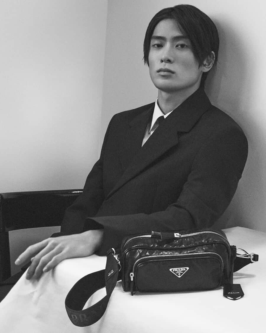 Asian model wearing a black suit and white shirt with a black leather Prada belt bag