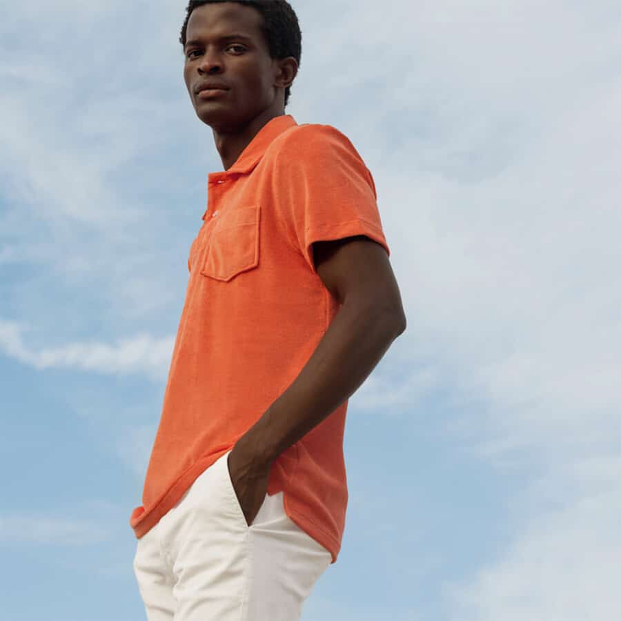 Black man wearing a bright orange luxury Aurélien terry towelling polo shirt with white pants