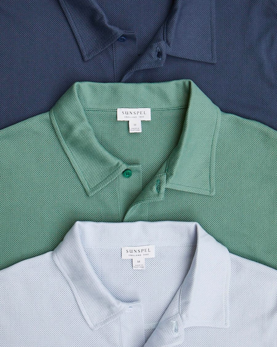 Three luxury Sunspel Riviera polo shirts in light blue, green and nay laid out on top of each other