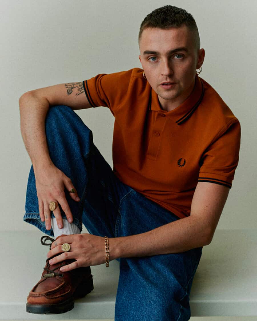 Man wearing a heritage Fred Perry orange-brown polo shirt with blue jeans, white socks and brown leather casual shoes
