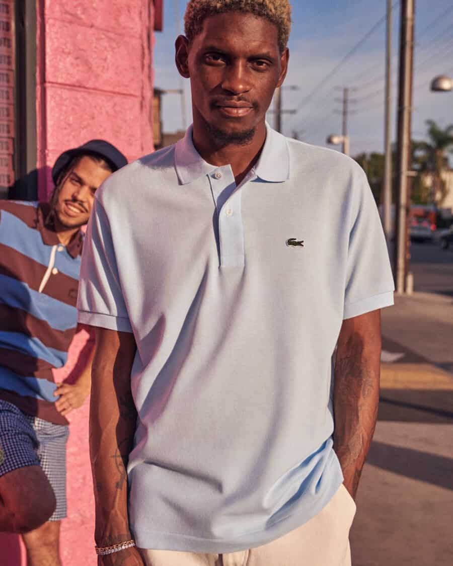Black man wearing a light blue Lacoste polo shirt and off-white pants