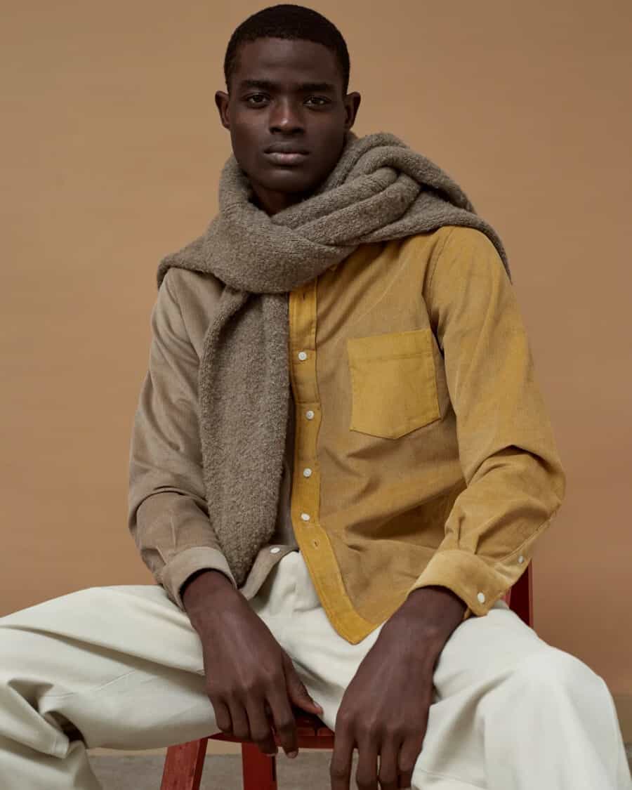 Black man wearing a high quality mustard yellow shirt, loose white pants and a brown knit sweater
