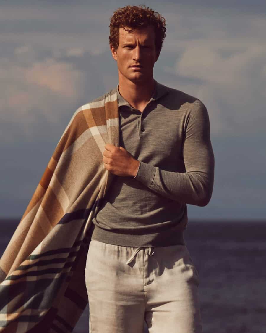 Man wearing high quality Johnstons of Elgin grey knitted long sleeve polo shirt and cream pants