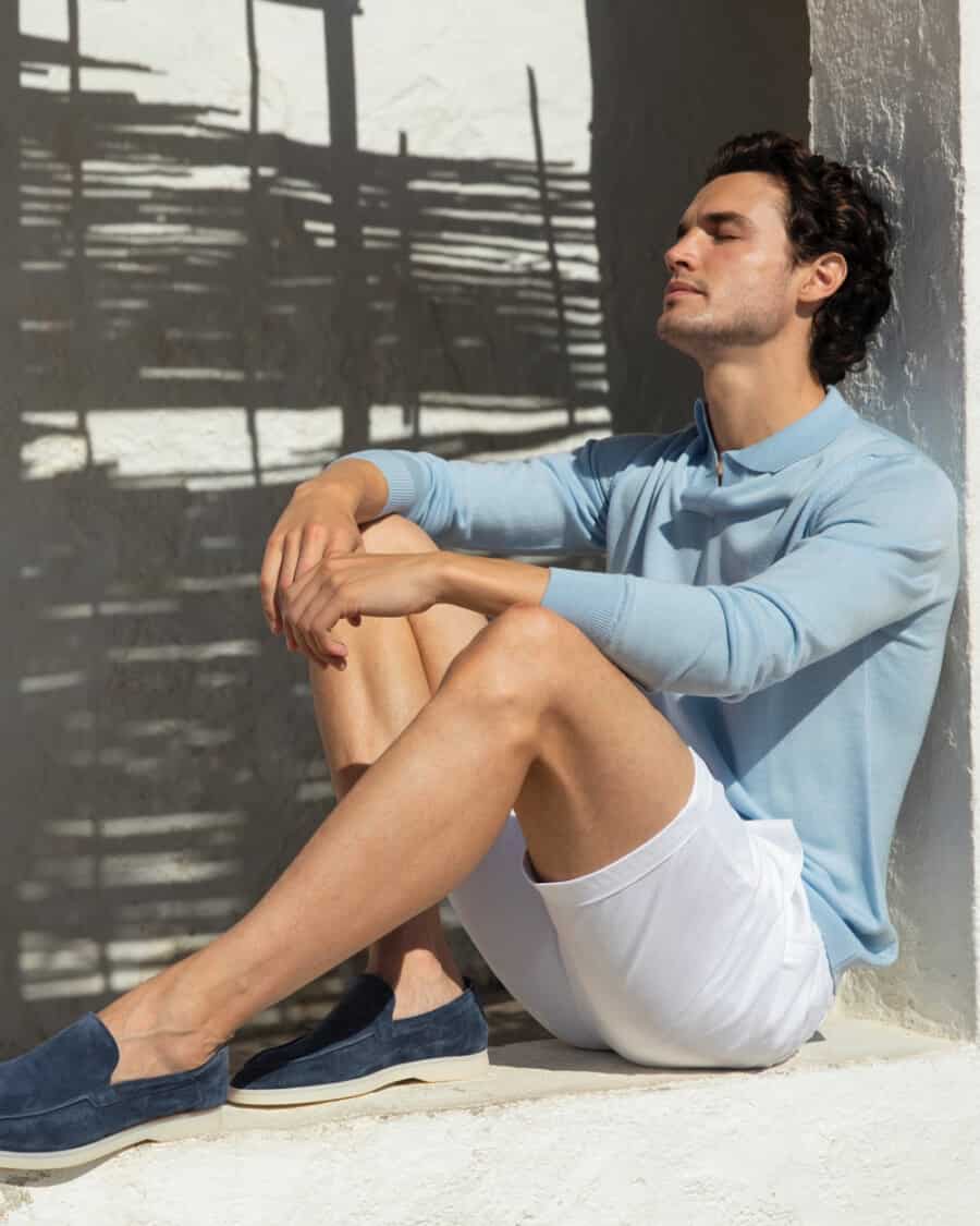 Man wearing high quality white shorts and a long sleeve light blue knitted polo shirt with navy suede loafers