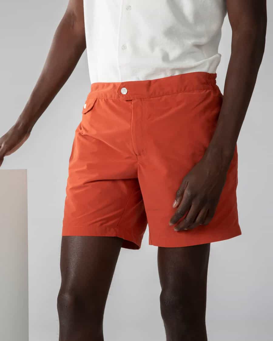 Man wearing bright orange tailored swimming shorts with a white T-shirt tucked into them