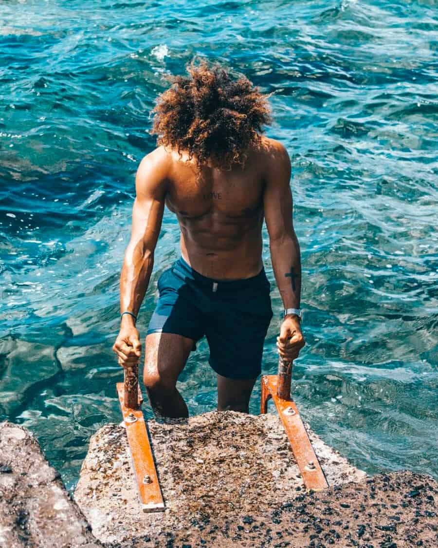 Black man climbing out of sea wearing a pair of navy tailored swimming shorts by Vilebrequin