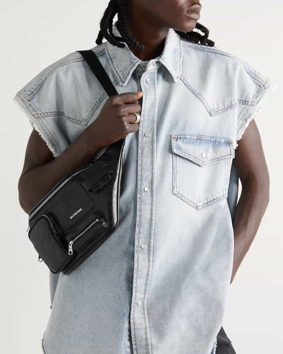Black man wearing a cutoff denim shirt and Balenciaga luxury black crossbody belt bag