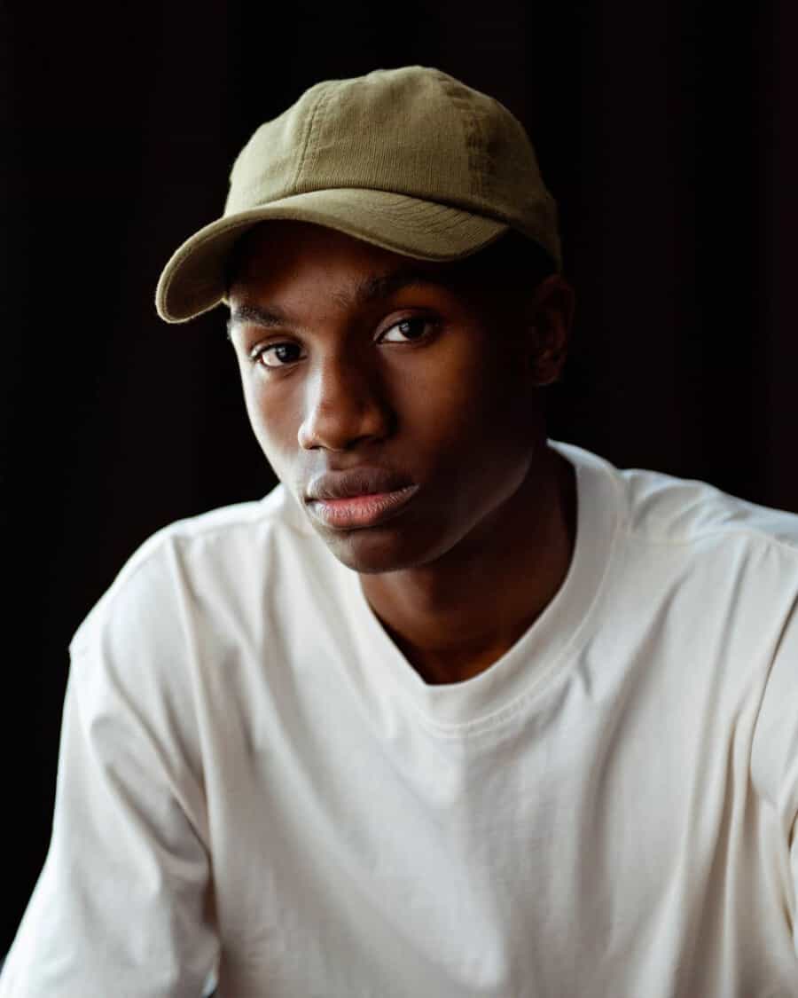 Black man wearing a fitted green baseball cap and long sleeve white top