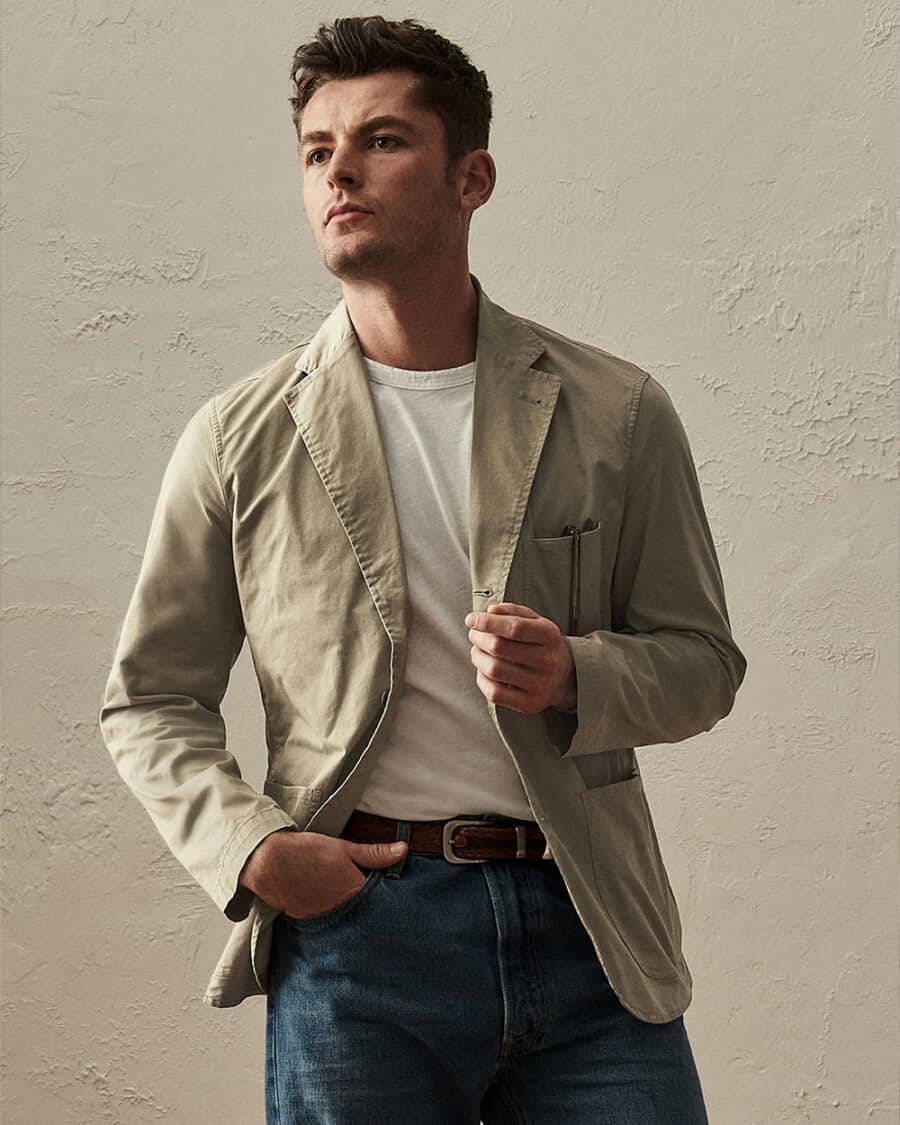 Man wearing white T-shirt with an unstructured cotton khaki blazer and blue jeans